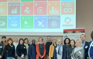 A group of people standing in front of a screen showing the UN's sustainability goals.